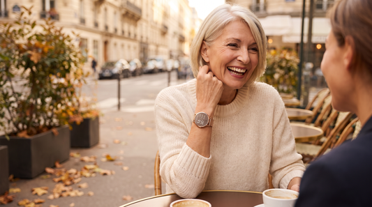 Une femme élégante de 60 ans rit en terrasse, la montre connectée L'Épurée au poignet