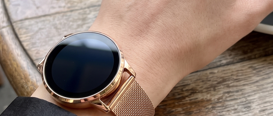 Montre connectée ronde or rose au poignet, avec un bracelet en maille : elle ressemble à une vraie montre